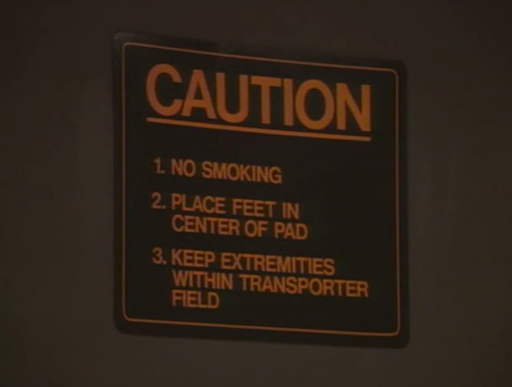 screencap of a sign that says CAUTION above a numbered list: 1. NO SMOKING, 2. PLACE FEED IN CENTER OF PAD, 3. KEEP EXTREMITIES WITHIN TRANSPORTER FIELD